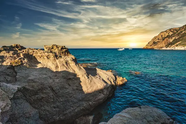 Cala sa figu 'daki Rocky sahili, sardunya, altın bir günbatımında turkuaz su ve botlarla