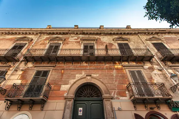Tarihi bir binanın yıkılan cephesi demir balkonlar ve yıpranmış kepenkler, Sicilya 'daki Falconara' nın özünü yakalıyor.