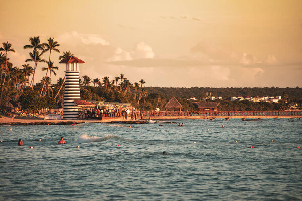 Туристы плавают и отдыхают на пляже доминик с его знаковым полосатым маяком на закате, в баяхибе, Доминиканская республика
