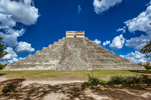 Meksika, Yucatan 'daki Chichen itza arkeolojik alanının ana piramidi El Castillo, tüylü beyaz bulutlarla kaplı canlı mavi gökyüzüne karşı dimdik ayakta duruyor.