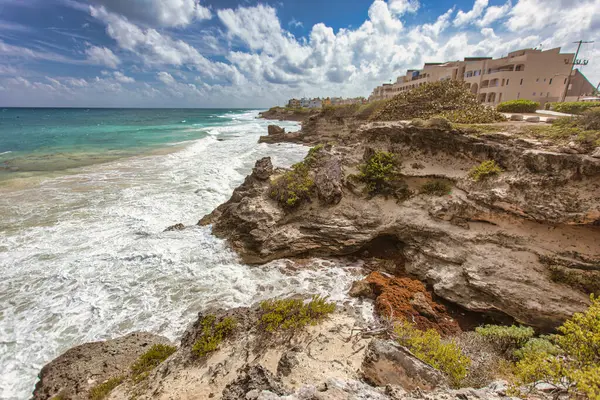 Turkuaz okyanus dalgaları Isla Mujeres, Meksika 'nın kayalık sahillerine çarpıyor. Arka planda bulutlu bir gökyüzünün altında bir tatil yeri var.