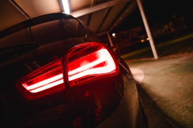 Automobile taillight illuminated in red and white colors at night, showcasing contemporary design and wet surface after rainfall, parked securely under a carport in the dark