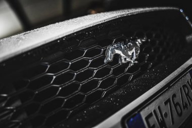 Rome, italy 30 september 2025: close-up ford mustang chrome horse grille glistening with raindrops, wet metallic detail reflecting light and sleek automotive design.