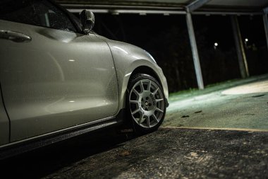 Rome, italy 30 september 2025: white suzuki swift sport hatchback with aftermarket wheels parked under dim urban lighting, wet body and reflections from rain nighttime