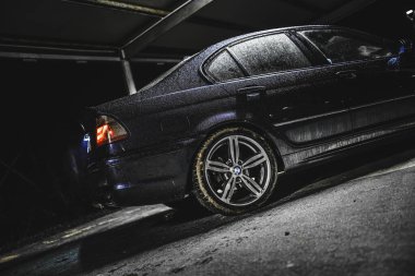 Rome, italy 30 september 2025: bmw sedan covered in rain and dirt, parked on a wet sloped asphalt surface in a dark indoor parking garage, moody low light