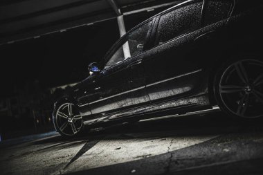 Rome, italy 30 september 2025: black bmw sedan glistening with rain drops, parked on wet asphalt in a moody, dimly lit urban parking lot at night