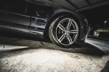 Rome, italy 30 september 2025: bmw alloy wheel and tire glistening with rain droplets on wet asphalt at night, low-angle urban mood and reflections