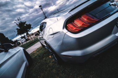 Rome, italy 30 september 2025: silver ford mustang coupe parked under dramatic cloudy sky, metallic sleek rear and iconic tri-bar taillights emphasizing power and design