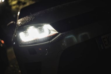 Rome, italy 30 september 2025: volkswagen golf gti headlight pierces rainy night, casting reflections and shimmering water-drop bokeh on wet urban road