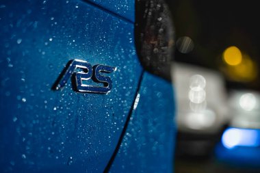 Rome, italy 30 september 2025: blue ford focus rs emblem glistening with raindrops at night, bokeh lights reflecting off wet metallic logo on urban street