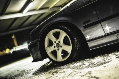 Rome, italy 30 september 2025: bmw white alloy wheel shot low-angle on wet garage floor at night, glossy tire and puddles under moody spotlight and rain droplets