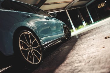 Rome, italy 30 september 2025: blue sports car glistening with rain droplets in a dimly lit urban parking lot at night, moody reflections on wet asphalt