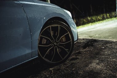 Rome, italy 30 september 2025: wet blue hyundai n sports car wheel at night on asphalt, close-up showing alloy rim, tire and red brake caliper reflections
