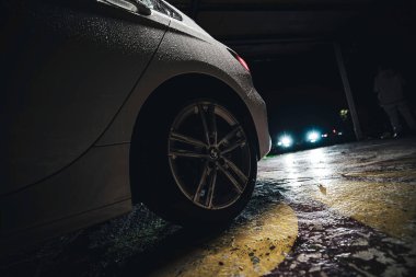 Rome, italy 30 september 2025: bmw wheel and wet exterior glistening under urban headlights on a dark rainy parking lot, dramatic reflections and moody bokeh