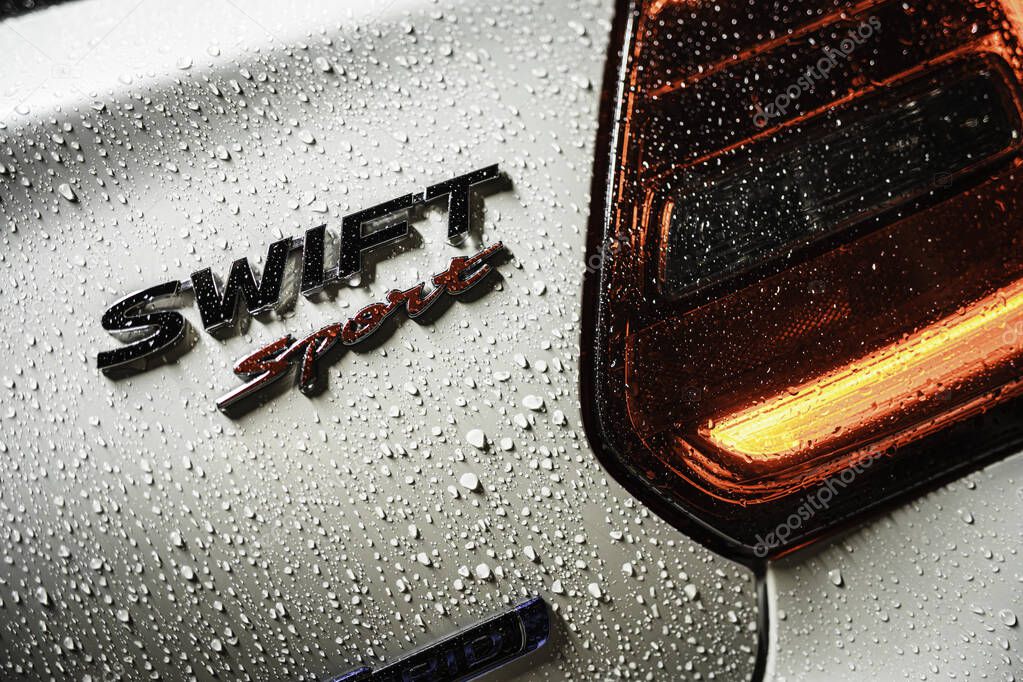 Rome, italy 30 september 2025: suzuki swift sport hatchback wet with rain droplets, close-up on illuminated taillight, badge and reflective silver paint texture