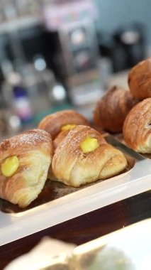 Close up view of freshly baked italian croissants, known as cornetti, and other pastries filled with custard and jam, elegantly displayed on trays inside a warm, inviting cafe showcase