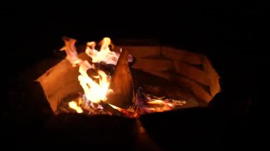 Crackling orange flames from burning wood logs in a stone fire pit create a warm and cozy atmosphere during a dark night, providing both heat and a relaxing light in the wilderness