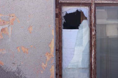 Eski bir torbayla asılmış ahşap bir çerçevenin kırık camı. Terk edilmiş eski bir evin dış görünüşü.