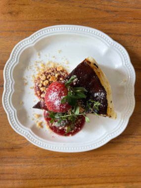 Bol çikolata soslu dilimlenmiş cheesecake, beyaz bir tabakta servis edilir ve taze çilekle süslenir.