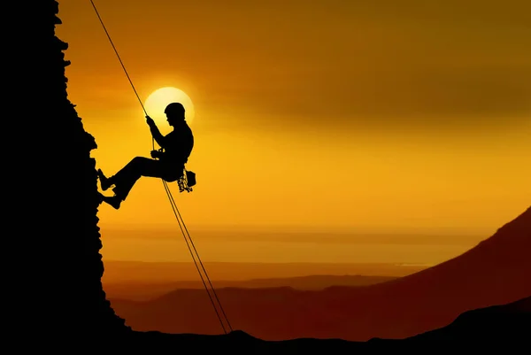 Silhouette of a rock climber on orange sunset background