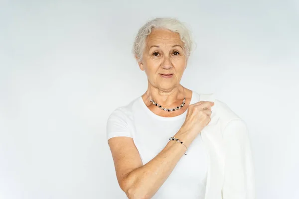 Happy senior grey hair woman portrait wearing white clothes showing jewellery bijouterie on white background.