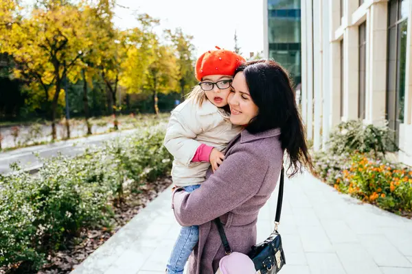 かわいい素敵なポジティブなブルネットの母親は 彼女の幸せな障害の娘を運んでいる 女性と子供は外で秋の晴れた日を散歩を楽しむ — ストック写真