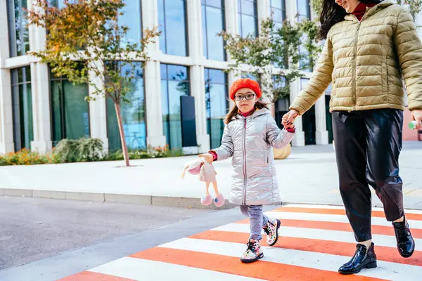 若い白人母親が通りを横断し 秋にメガネと赤いベレーを身に着けている小さな娘と町の中心街を歩いている フルハイト — ストック写真