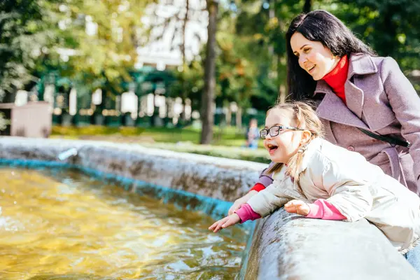 幸せな家族の瞬間コンセプト カラフルなカフカシウマと小さな女の子の子供は 楽しみを持っています 晴れた公園で噴水の屋外の水で遊びます — ストック写真