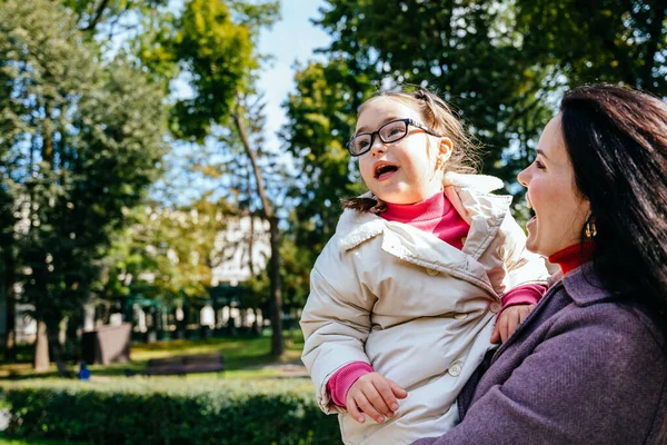特別なニーズを持つ小さな女の子は 屋外の公園で母親と過ごす時間を楽しんでいます かわいい表情の眼鏡で素敵な子供 — ストック写真