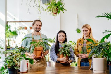Çiçekçide yoğun bir iş günü. Ağaç işçileri, Asyalı kadın, yakışıklı erkek ve orta yaşlı başarılı sarışın kadın sahibi yeşil alanda farklı bitkiler tutuyor..