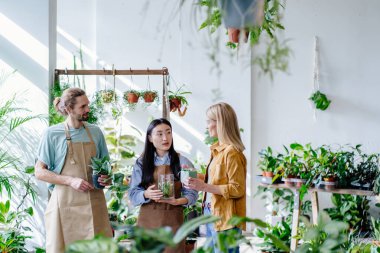 İki mutlu işçi, erkek ve kadın bahçıvan gibi giyinmiş bir tencere, dekor ve çiçekçi modern iç mekanda bir kadın müşteriye hizmet ediyor. Fabrika işi, başlayın..