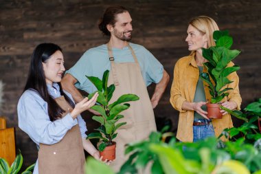 Çiçekçi dükkanının modern iç mekanında çiçeklerle ilgili bilgisi olan iki çiçekçi kadın müşteriye yardım ediyor. Küçük işletme, ev dekorasyonu konsepti. Fabrika işi, başlayın..