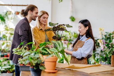 Çekici Asyalı çiçekçi bahçıvan bir çiçekçide iki alıcıya yardım ediyor. Fabrika işi, başla. Küçük işletme kavramı.