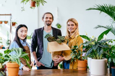 Saksıda ev bitkileri satmak. Genç Asyalı mutlu çiçekçi dükkanının portresi çiçekçi dükkanında müşterisine yardım ediyor. Fabrika işi, başlayın..