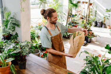 Önlük takan yakışıklı beyaz adam çiçekçide yeşillik özenle saksı bitkisini kağıda sarıyordu. Samimi çiçekçideki işinden zevk alıyor. Şehir ormanı ve bitki ebeveyni kavramı.
