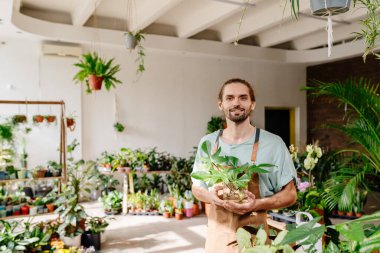 Genç beyaz sakallı, çiçekçi dükkanı sahibi. Çiçekçi dükkanında kendine gülerek duruyor..