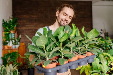 Kafkasyalı genç bir bahçıvanın portresi. Önlük takıyor. Çiçeklerle ilgileniyor. Çiçekçilik ve insanların konsepti.