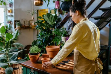 Çiçek, iş, dekorasyon konsepti. Genç Afro-Amerikan ilham verici kadın, modern çiçekçi dükkanında önlük giyiyor..