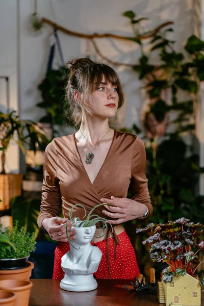植物店の花屋で現代の鍋で土なしで簡素な植物と働く慎重な女性アシスタントの垂直ショット — ストック写真