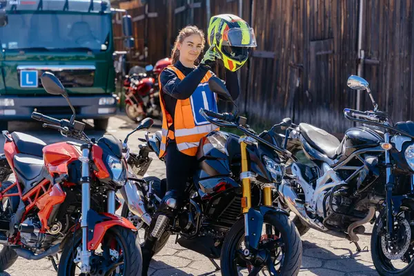 Stock image A woman puts a motorcycle helmet on motordrome with other motorcycles. Concept of motorcycle school of driving, as the woman is likely preparing for a ride or has just finished one.