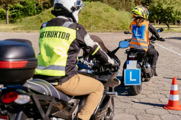 Stock image A man in a yellow jacket is riding a motorcycle with a blue license plate. He is being followed by a man in a black jacket