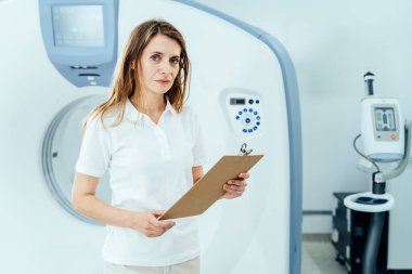 MRI tarayıcısının önünde duran kadın teknisyenin portresi.