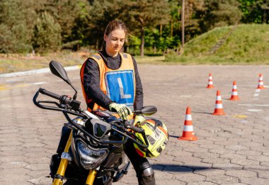 Moto Okulu hipodrom sürüş okulu. Motosiklet konseptini öğreniyorum. Kadın L-driver koniler arasında araba kullandıktan sonra rahatlıyor, motosiklet okulu dersi.