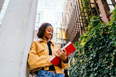 Eğitim, okul ve insan konsepti. Kitapları olan siyahi bir kadın kampüste duruyor..