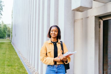 Gülümseyen Afrikalı Amerikalı kadın öğrenci egzersiz kitapları ve sırt çantası, eğitim, okul ve insanların konseptini tutuyor..