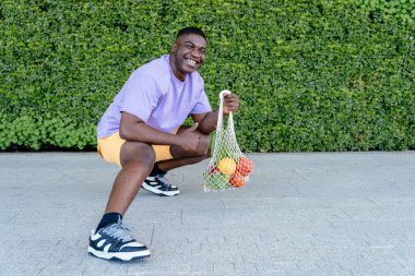 Sürdürülebilirlik, gıda alışverişi ve çevre dostu konsept. Afrikalı siyahi adam plastik paketli ağ torbası kullanıyor..