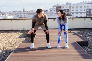 Neşeli çift yaz sabahı şehir manzarasına karşı eğitime hazırlanıyor. Mutlu spor çifti, binanın terasında sağlık jimnastiği yapıyor..