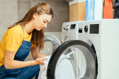 Çamaşır makinesinin içinde banyo zemininde kirli çarşaflara bakan yorgun bir kadın. Kızgın kadın yorgunluğu, depresyon ve kriz temizlik sorunu, felaket ve sorun