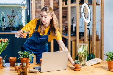 Serbest meslek. Çevrimiçi dersler. Küçük işletme konsepti. Profesyonel Asyalı kadın bahçıvan evde dizüstü bilgisayar ve telefon kamerasıyla bitki saksıları düzenleme sınıfında vlog oturumu yapıyor..