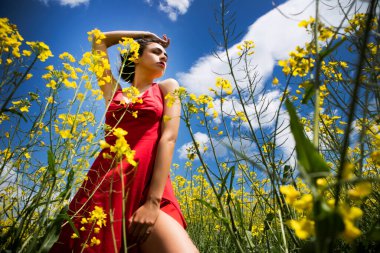 Young girl dressed in red dress in a field of yellow flowers in summer season 